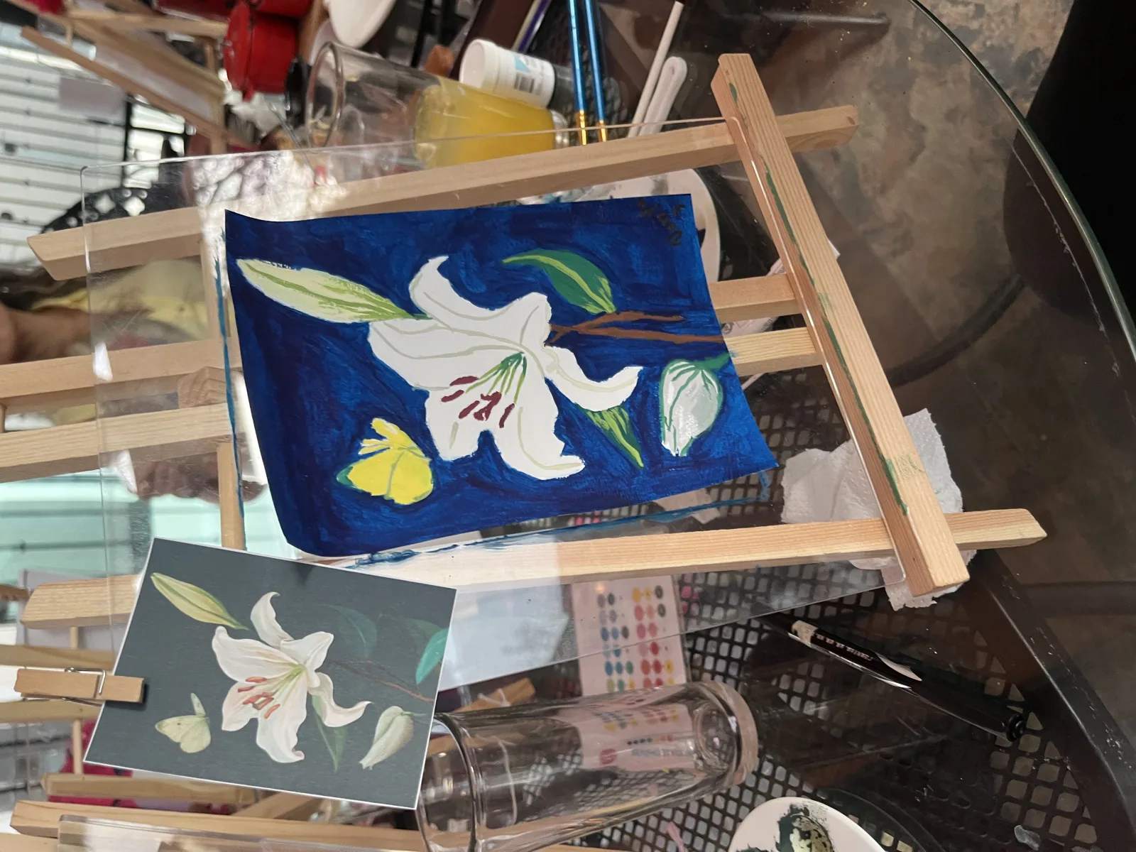 Pintura de azucenas blancas sobre fondo azul terminada en un caballete