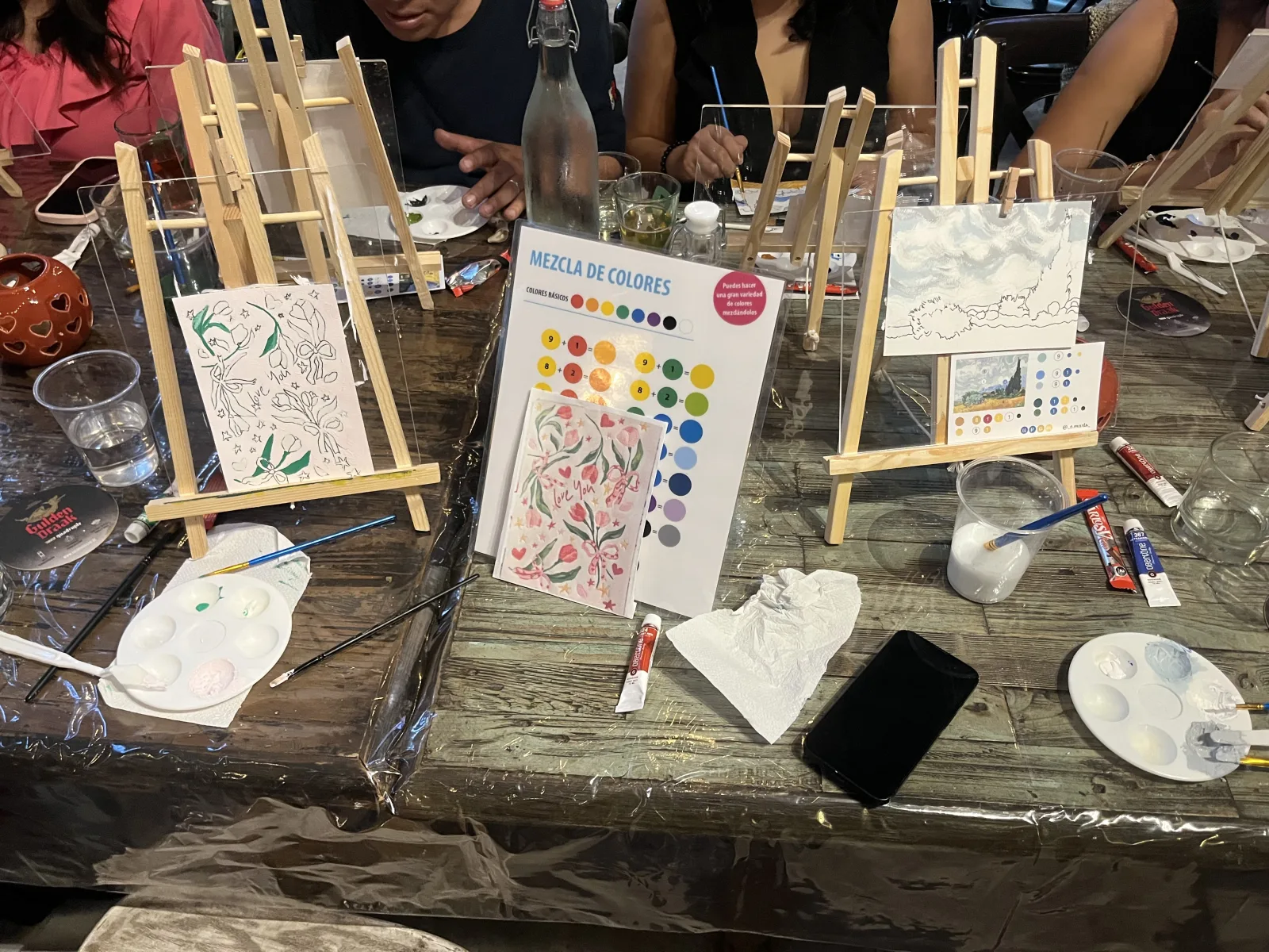 Mesa de taller con caballetes, paletas y una guía de mezcla de colores