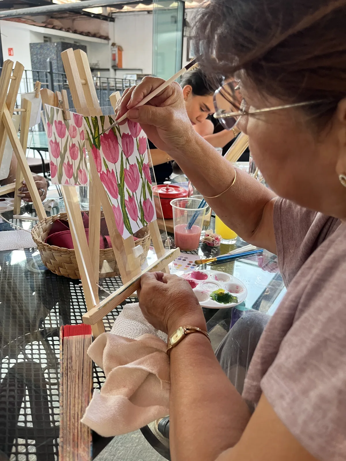 Una asistente pinta tulipanes rosas en gouache sobre un lienzo pequeño